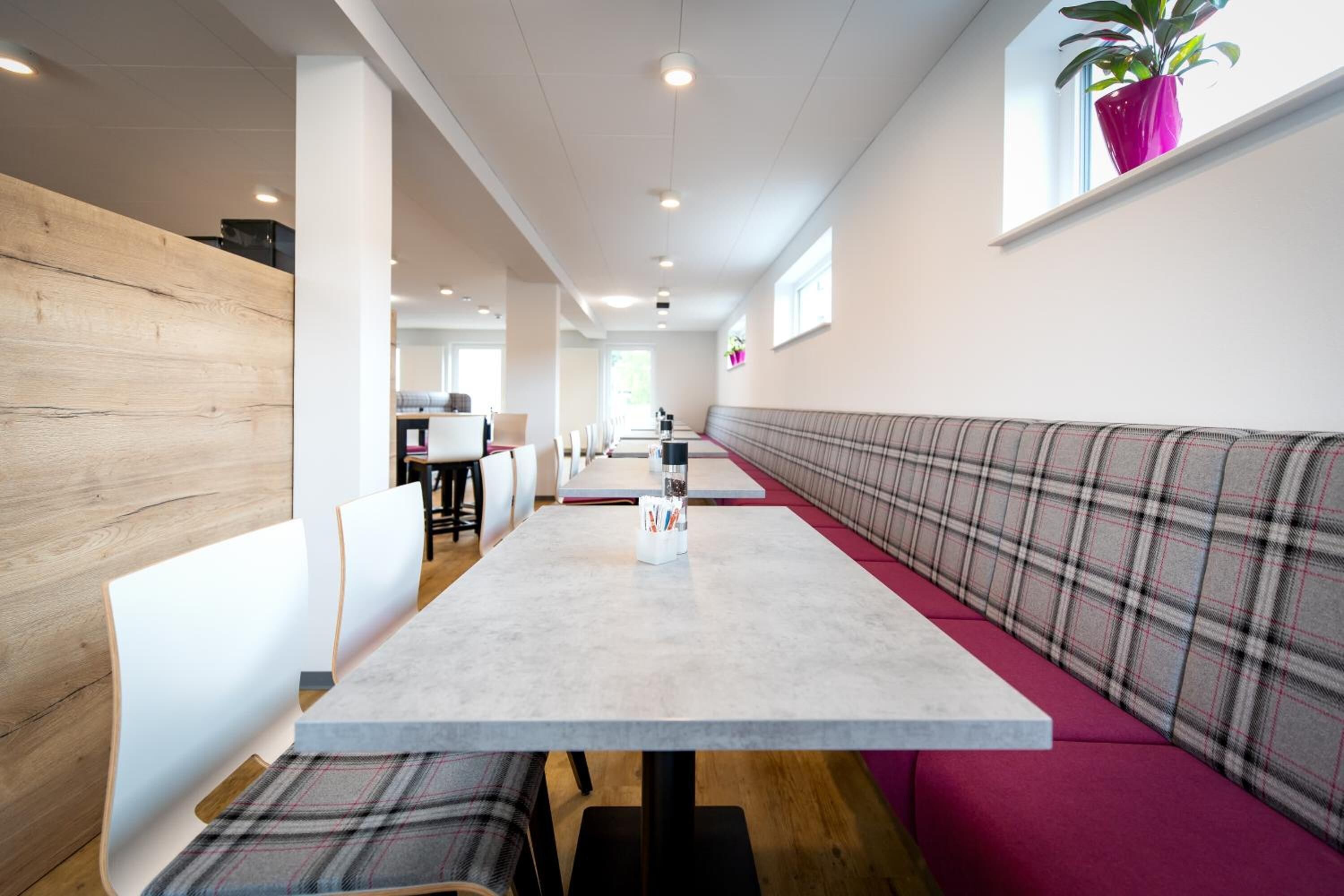 A modern restaurant with a long dining table, white chairs, and a bench with plaid upholstery.