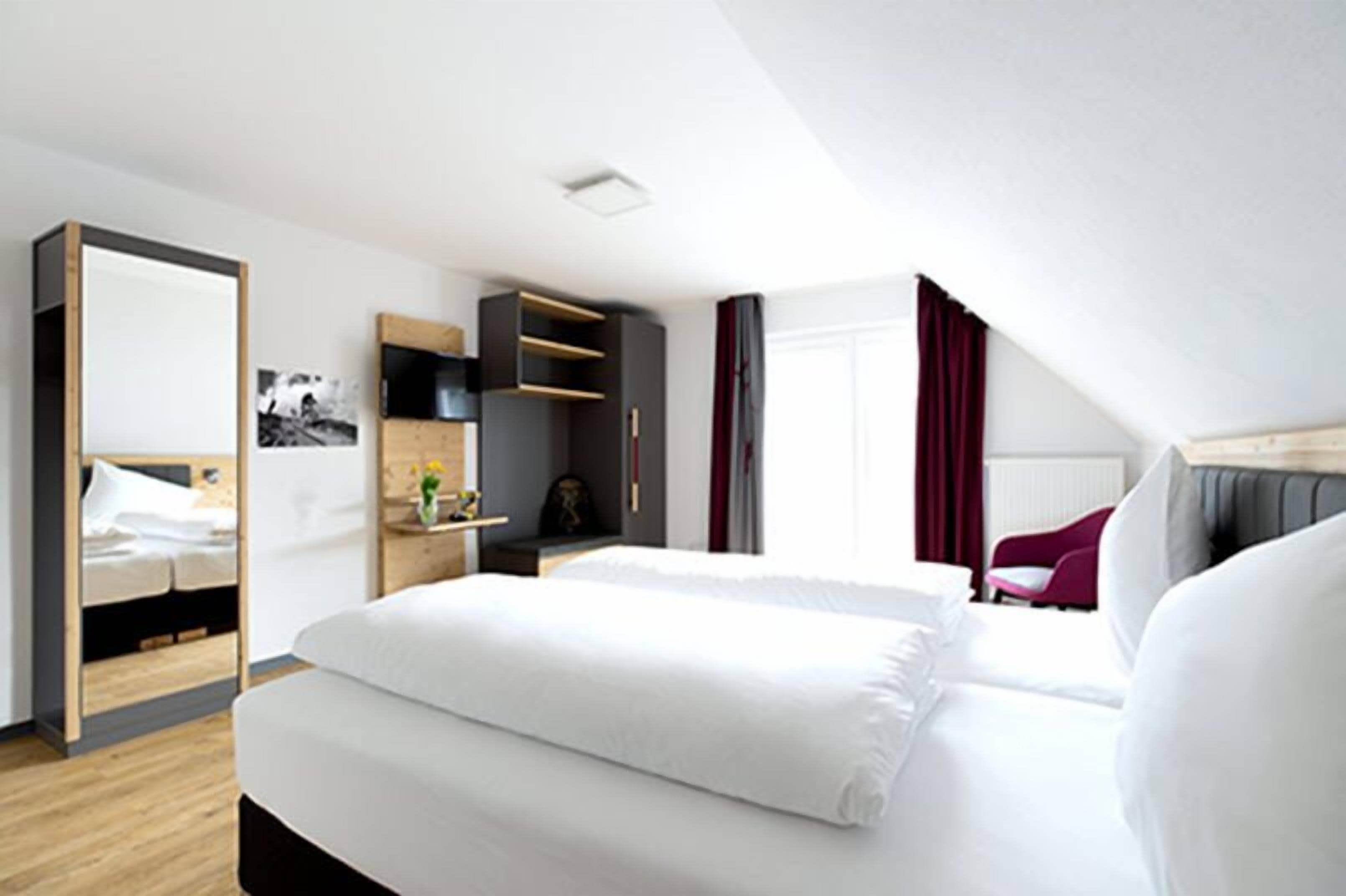 A modern hotel room with a large bed, a desk, and a wardrobe.