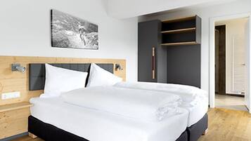 A modern hotel room with a wooden headboard, a large bed with white linens, a gray wardrobe, and a framed picture on the wall.