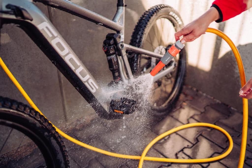A person cleaning a bicycle with a water hose.
