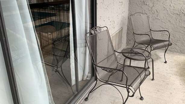 A balcony with two metal chairs and a table, a sliding glass door, and a textured wall. - Olde Gatlinburg 203 is a beautiful condo with private balcony located in downtow (Gatlinburg)