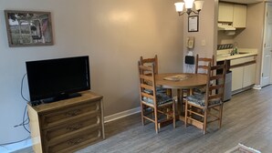 A dining area with a wooden table and chairs, a television on a wooden cabinet, and a kitchen in the background. - Olde Gatlinburg 203 is a beautiful condo with private balcony located in downtow (Gatlinburg)
