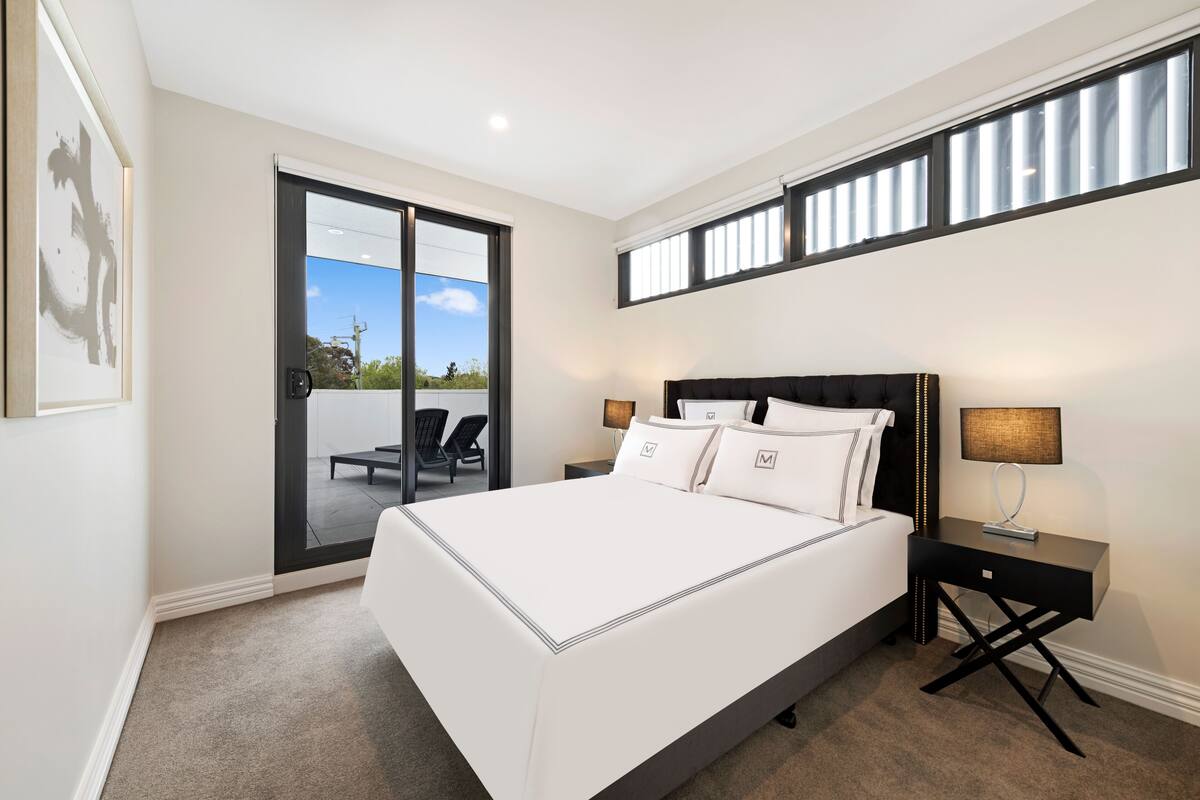 A bedroom with a large bed, a nightstand, a lamp, and a sliding glass door leading to an outdoor area.