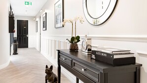 En hall med ett svart konsolbord, en rund spegel, inramade tavlor och en liten hund.