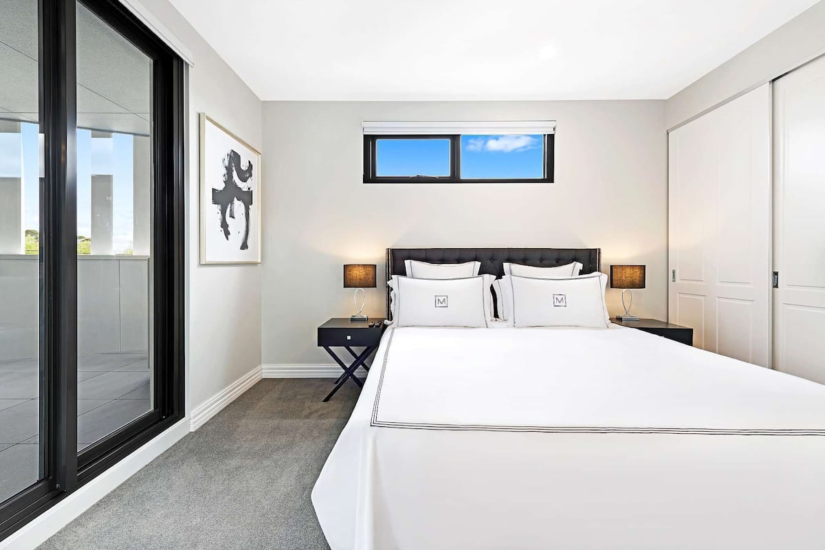 A hotel room with a large bed, two bedside tables, a window, and a framed artwork on the wall.