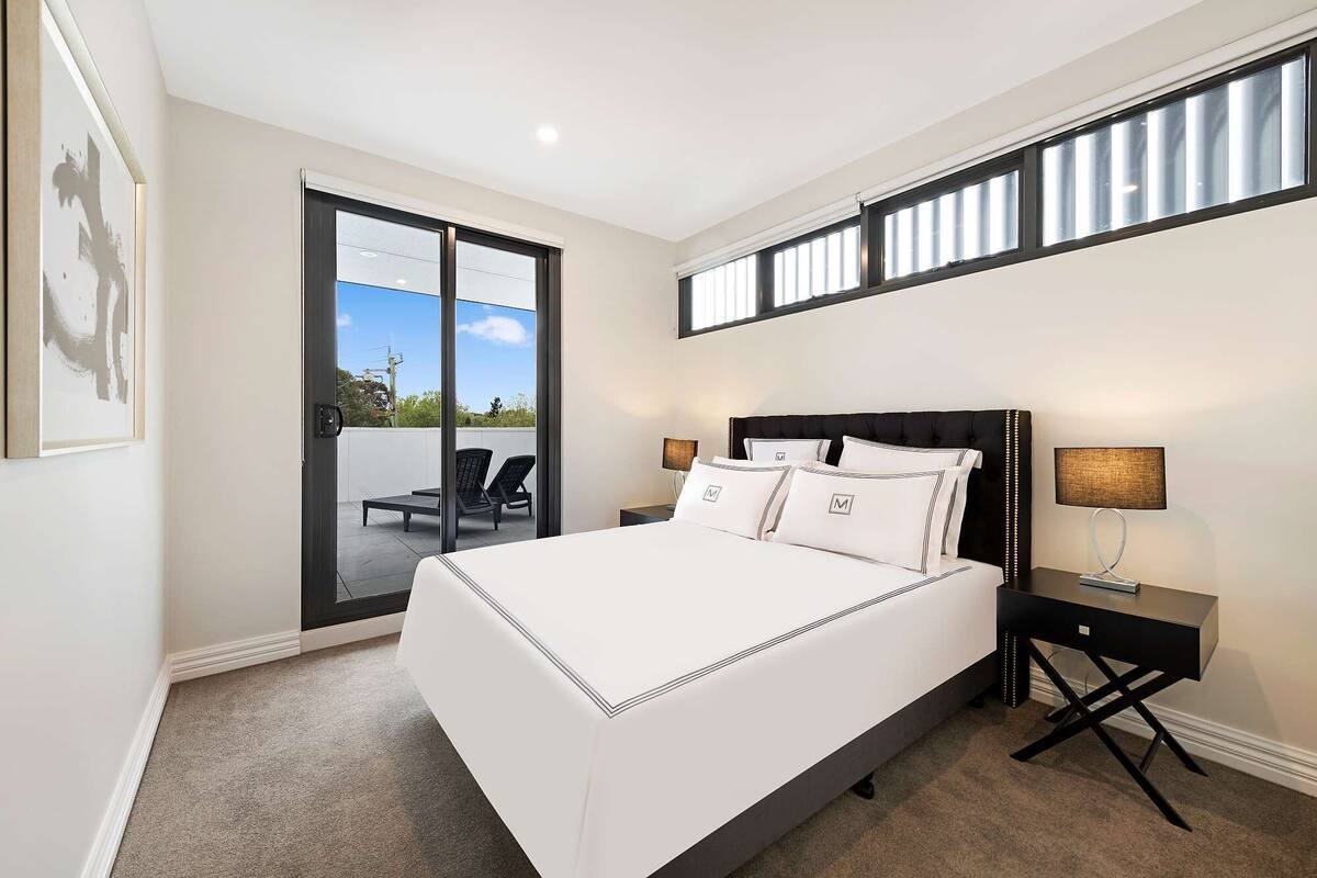 A bedroom with a large bed, a nightstand, a lamp, and a view of the outdoors through a sliding door.