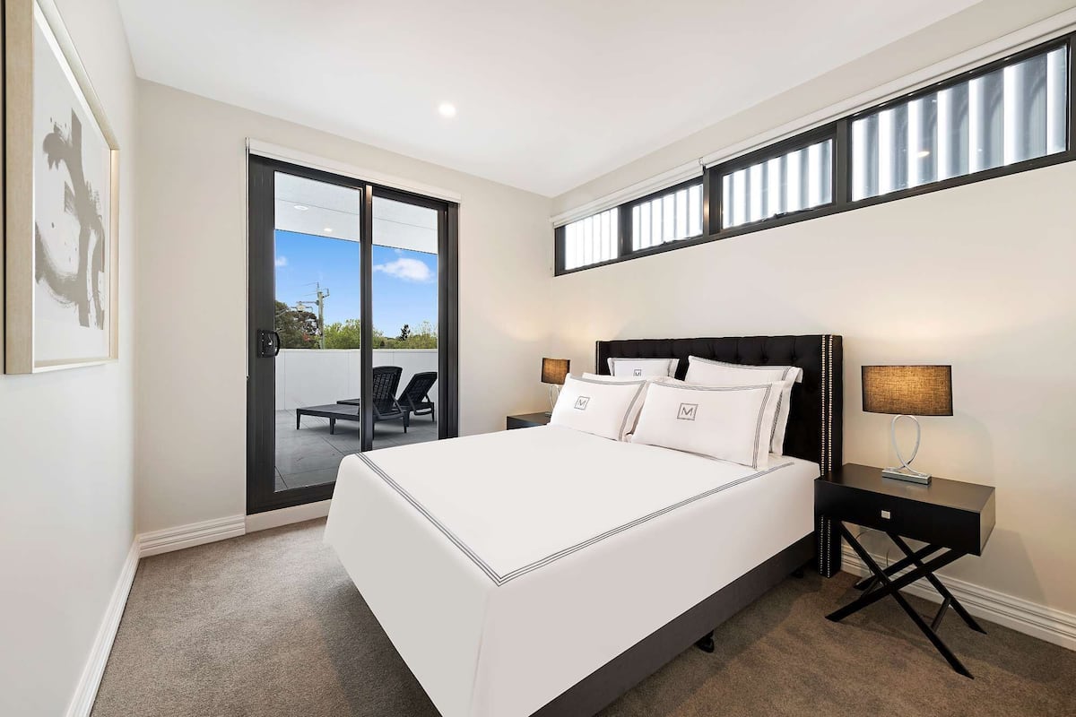 A bedroom with a large bed, a nightstand, a lamp, and a view of the outdoors through a sliding door.