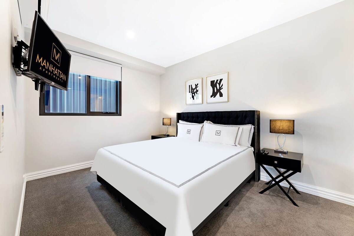 Une chambre d’hôtel moderne avec un grand lit, deux tables de chevet, un panneau suspendu et des œuvres d’art au mur.