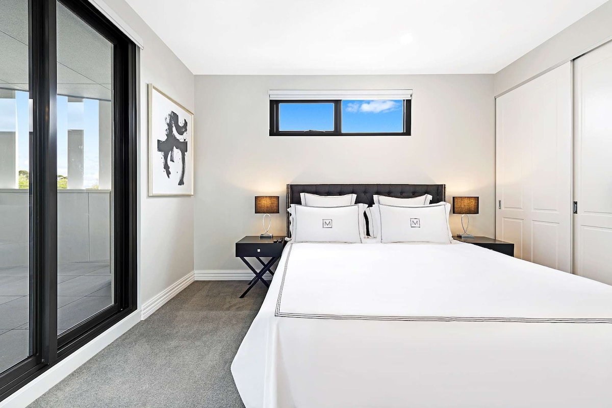 A hotel room with a large bed, two bedside tables, a window, and a framed artwork on the wall.