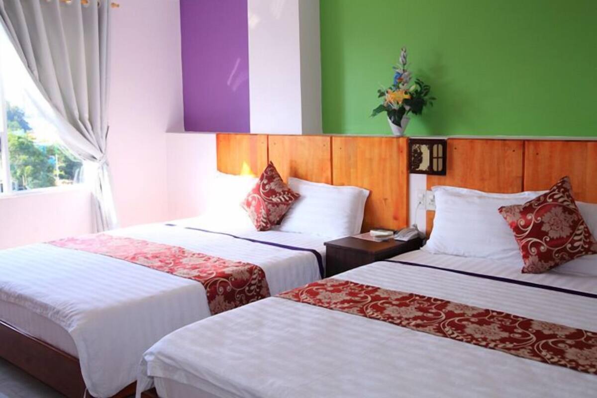 A hotel room with two beds, a wooden headboard, a green accent wall, and a window with curtains.