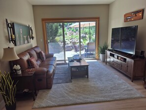 A living room with a sofa, coffee table, TV, and a view of a patio with outdoor furniture. - Holiday time in beautiful Bend! Awesome house, chef's kitchen, serene backyard  (Bend)