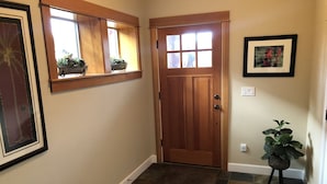 A hallway with a wooden door, a window with plants, a rug, and a framed picture on the wall. - Fall hiking & mtn biking from front door! Large Chef's kitchen, serene backyard  (Bend)