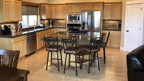 A modern kitchen with wooden cabinets, stainless steel appliances, and a central island with bar stools. - Fall hiking & mtn biking from front door! Large Chef's kitchen, serene backyard  (Bend)