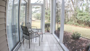 A covered porch with two chairs and a small table, a sliding glass door leading to a garden. - 1st Floor! Corner Unit! 3 Bedrooms! True Blue Golf Course, Minutes from Beach! (Pawleys Island)