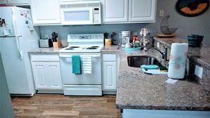 A kitchen with white cabinets, a stove, a microwave, a sink, and a countertop with various items. - 1st Floor! Corner Unit! 3 Bedrooms! True Blue Golf Course, Minutes from Beach! (Pawleys Island)