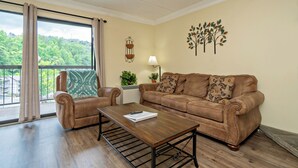 Una sala de estar con un sofá de cuero marrón, dos sillones, una mesa de centro de madera y vista a zonas verdes.