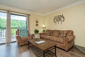Una sala de estar con un sofá de cuero marrón, dos sillones, una mesa de centro de madera y vista a zonas verdes.