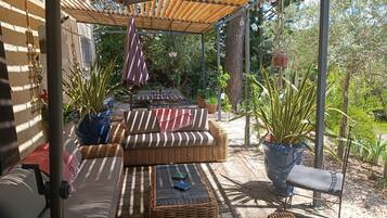 An outdoor patio with wicker furniture, potted plants, and a pergola providing shade.