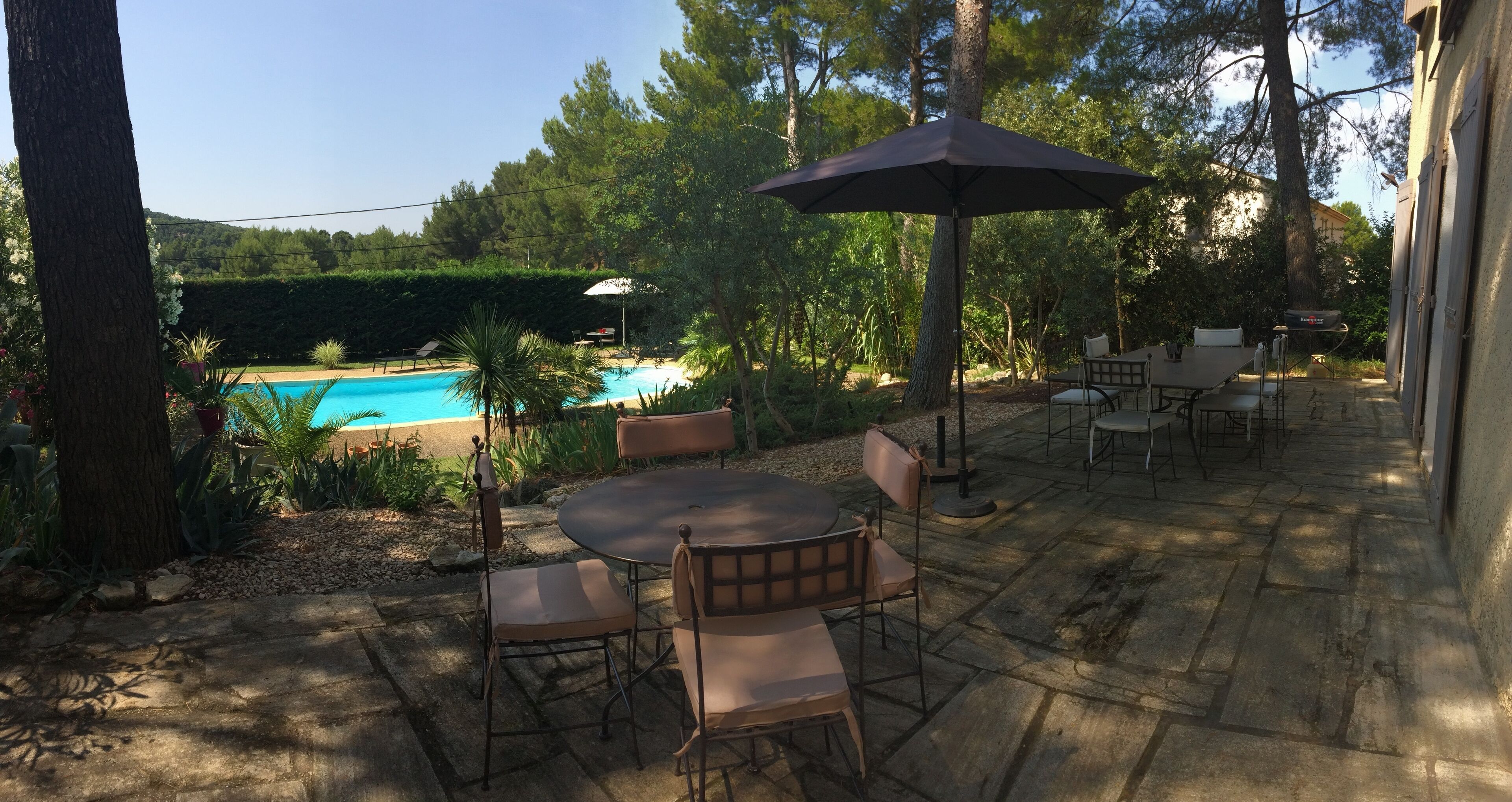 An outdoor patio with a pool, surrounded by trees and a stone floor.
