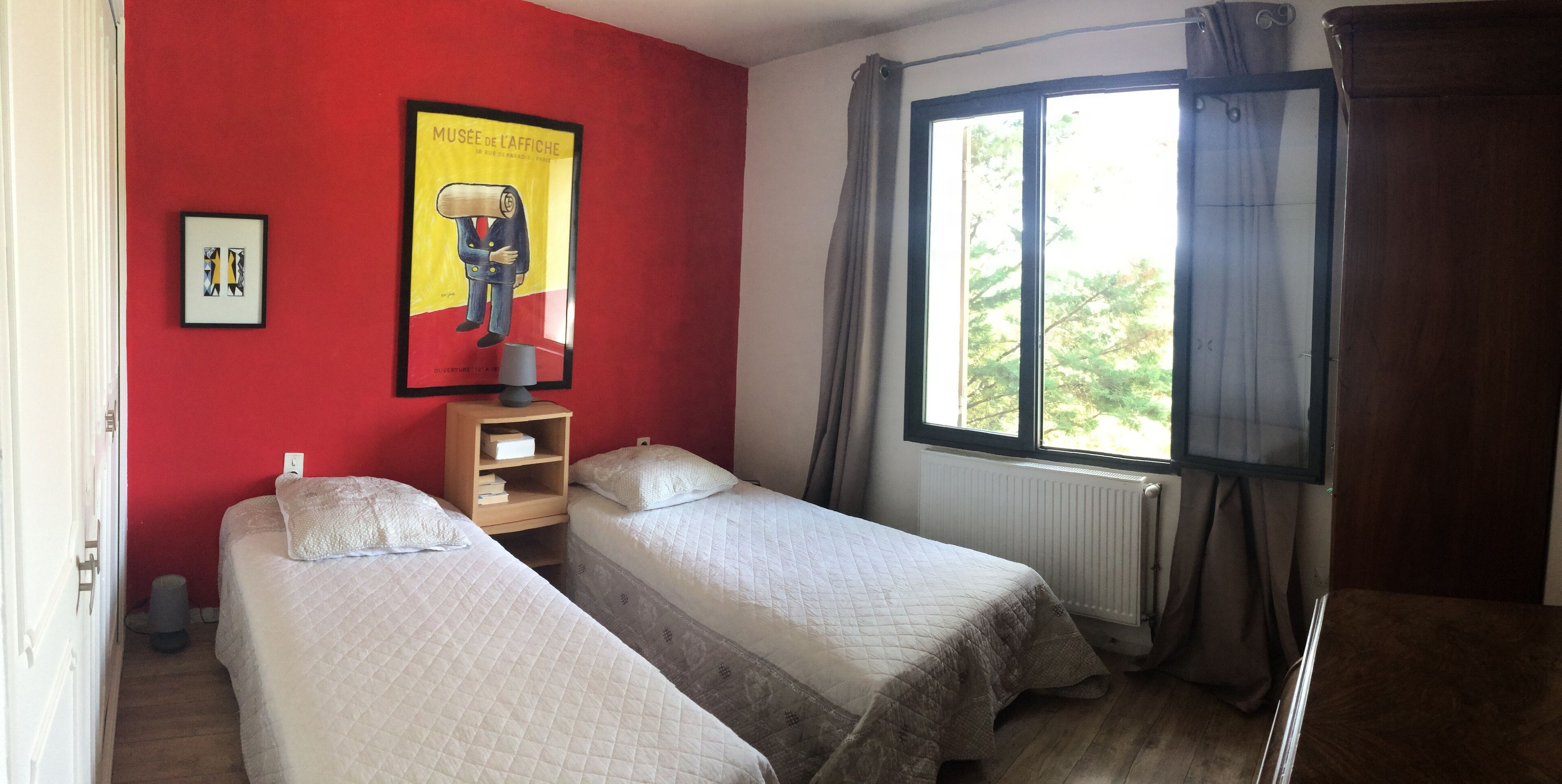 Une chambre avec deux lits, une fenêtre avec des rideaux, un radiateur et une affiche accrochée au mur.