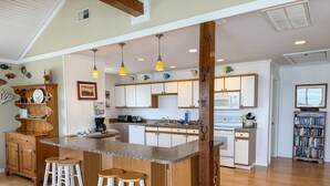 A spacious kitchen with a central island, wooden bar stools, and pendant lighting. - Badger Bungalow:  Sunsets over Pamlico Sound, private boat dock. (Ocracoke)