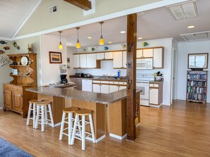Une cuisine spacieuse dotée d’un îlot central, de tabourets de bar en bois et de luminaires suspendus.