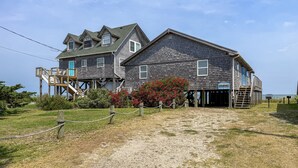 A two-story wooden building with a staircase leading to a deck, a sign indicating a restaurant, and a sandy path in front. - Badger Bungalow:  Sunsets over Pamlico Sound, private boat dock. (Ocracoke)