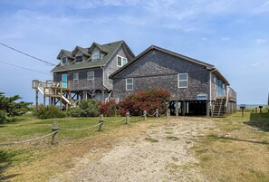 Un bâtiment en bois à deux étages, avec un escalier menant à une terrasse, une enseigne indiquant un restaurant et un chemin de sable devant.