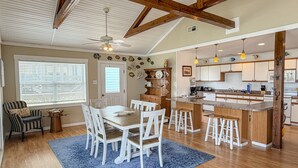 A spacious kitchen with wooden beams, a dining area with white chairs, and a blue patterned rug. - Badger Bungalow:  Sunsets over Pamlico Sound, private boat dock. (Ocracoke)