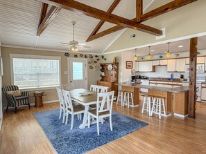 Une cuisine spacieuse avec des poutres en bois, un coin repas avec des chaises blanches et un tapis à motifs bleus.