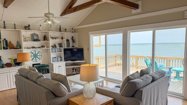 A living room with a TV, sofa, and a view of the ocean. - Badger Bungalow:  Sunsets over Pamlico Sound, private boat dock. (Ocracoke)
