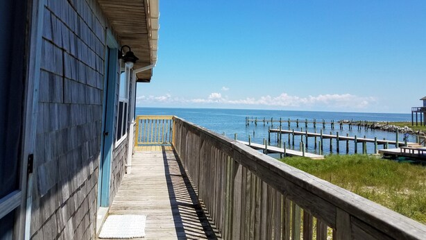 A wooden deck leading to a pier extending into the water, with a clear view of the ocean and a distant shoreline.