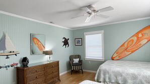 A bedroom with a bed, a dresser, a chair, a ceiling fan, and a window with blinds.