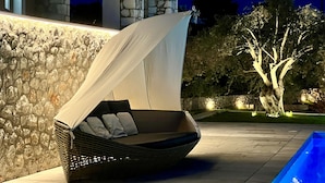 A modern outdoor seating area with a wicker chair and a canopy, set against a stone wall and a tree. - Villa Victory Porto Heli (Ermionida)