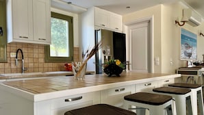 A modern kitchen with a large island, white cabinets, a tiled backsplash, and a window. - Villa Victory Porto Heli (Ermionida)