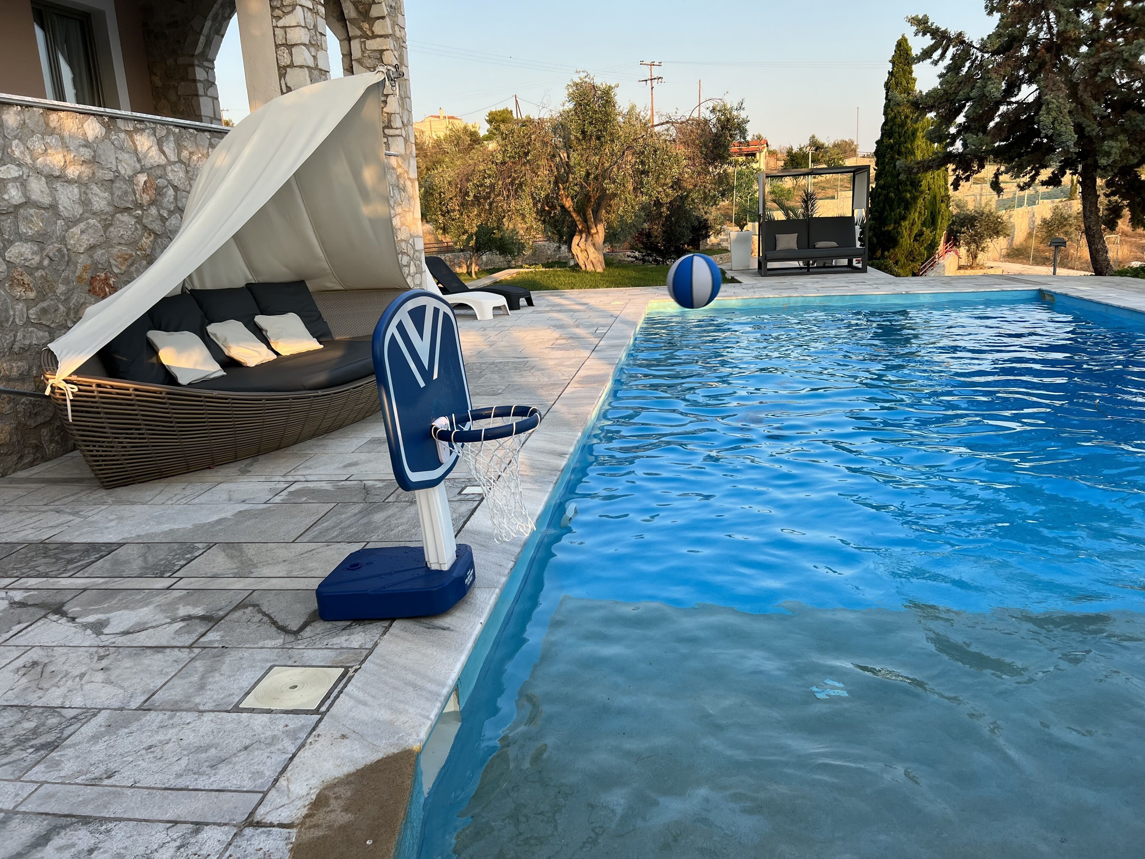 A pool area with a lounge chair, a small basketball hoop, and a stone wall.