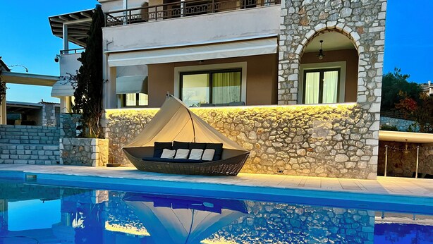 A pool with a boat-shaped lounge chair and a stone wall. - Villa Victory Porto Heli (Ermionida)