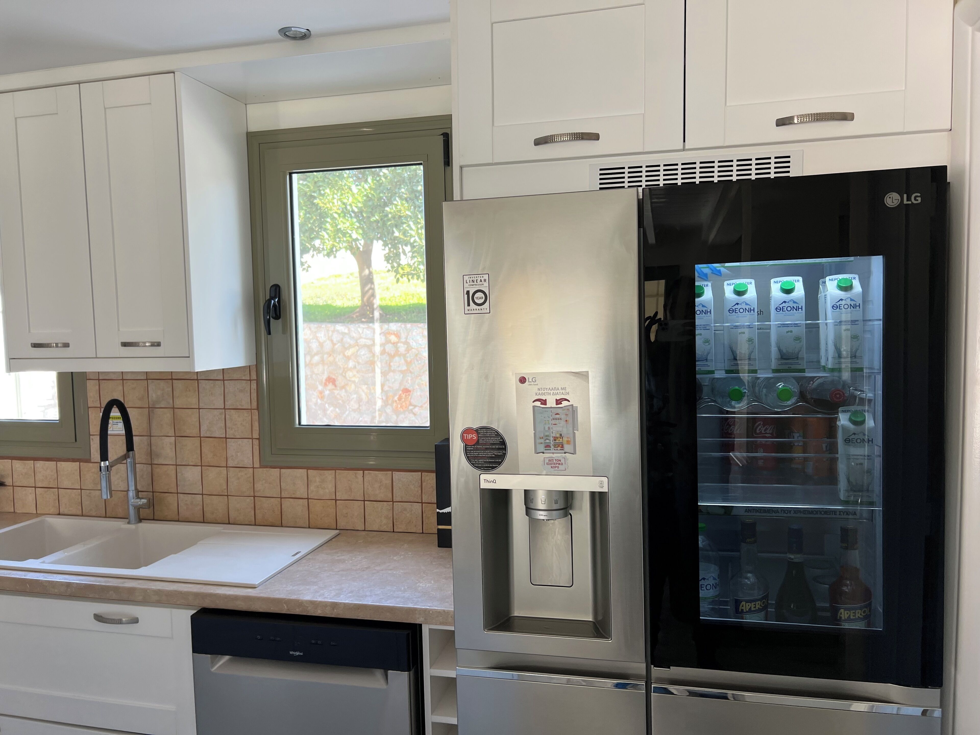 Une cuisine moderne avec des meubles blancs, un réfrigérateur GEONH encastré, un distributeur d’eau et un lave-vaisselle.