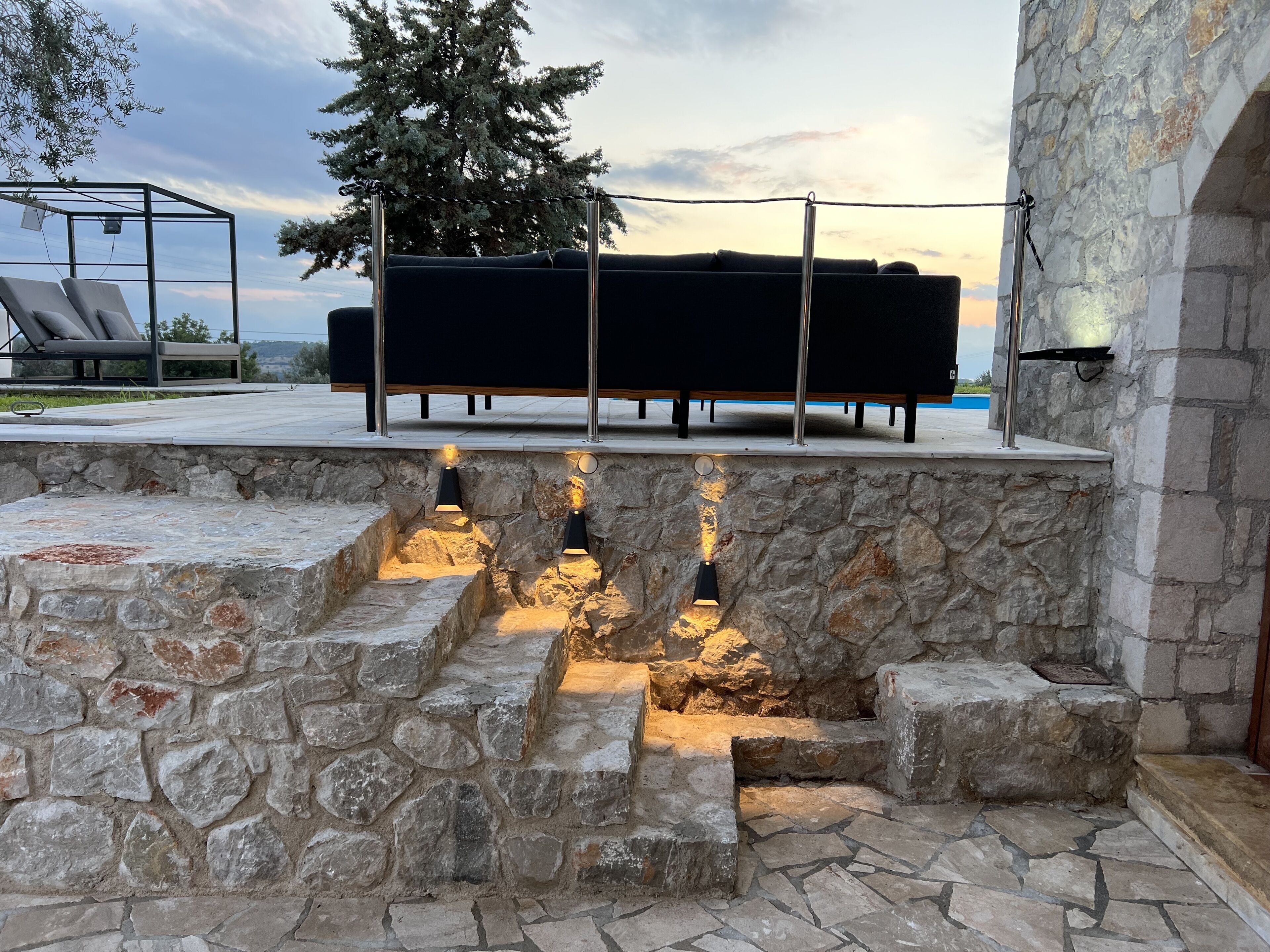 A stone wall with steps leading to a seating area with a black sofa and metal poles.