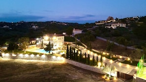 A large, well-lit villa with a swimming pool, surrounded by landscaped gardens and a view of a hilly landscape. - Villa Victory Porto Heli (Ermionida)