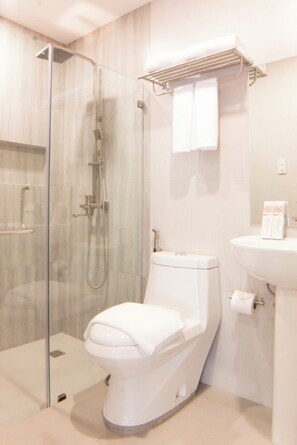 A modern bathroom with a glass-enclosed shower, a toilet, and a sink with a towel rack above. - Hotel Rosita (Lucena)