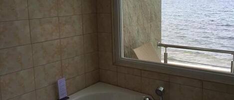 A bathroom with a large bathtub, a window with a view of the sea, and tiled walls.