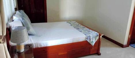 A neatly made bed with a wooden frame and a white mattress, a bedside lamp, and a floral bedspread.
