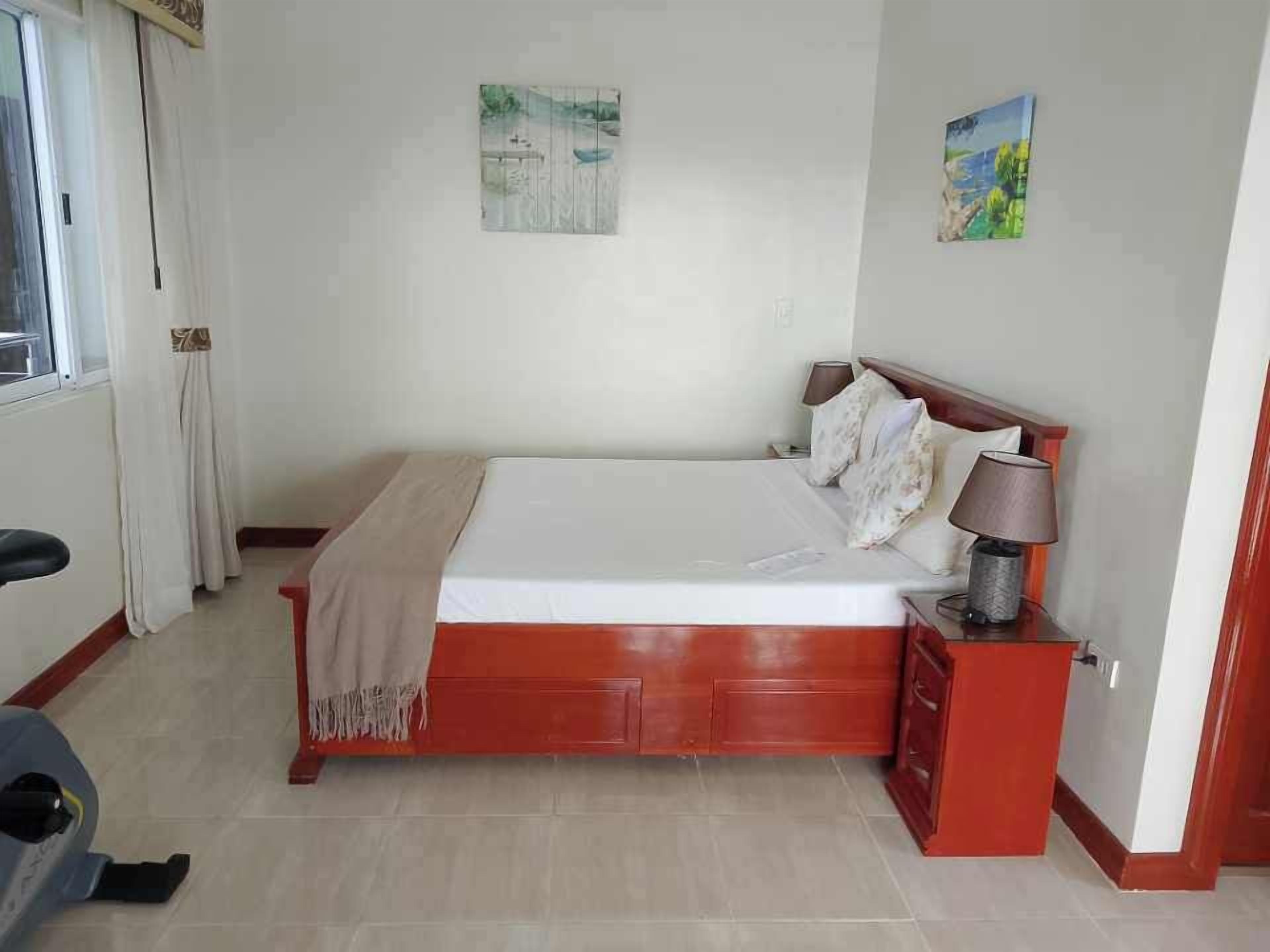 A bedroom with a bed, a nightstand, a lamp, and a window with curtains.