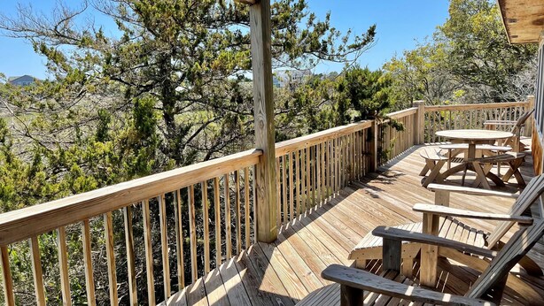 Eine Holzdielen-Terrasse mit Picknicktischen und -stühlen, umgeben von Bäumen.