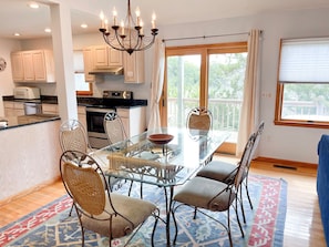 A modern kitchen with white cabinets, a microwave, and a stove. There is a dining area with a glass table and wicker chairs.