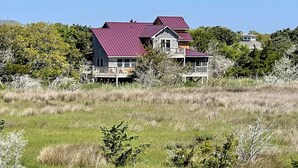 Ein großes, mehrstöckiges Haus mit rotem Dach, umgeben von einer grünen Wiese und dichten Bäumen.