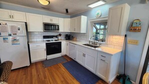 A kitchen with white cabinets, a microwave, stove, dishwasher, and a sink. - Wild Peony:  Incredible views from the ever popular rooftop deck! (Ocracoke)