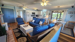 A cozy living room with a sofa, chairs, and a coffee table. There is a kitchen area with cabinets and a refrigerator. - Wild Peony:  Incredible views from the ever popular rooftop deck! (Ocracoke)