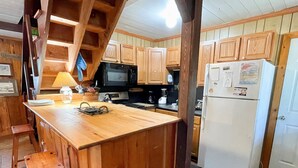 A kitchen with wooden cabinets, a microwave, a refrigerator, and a wooden island with stools. - Happy Place:  Pet friendly, fenced rear yard with deck. (Ocracoke)